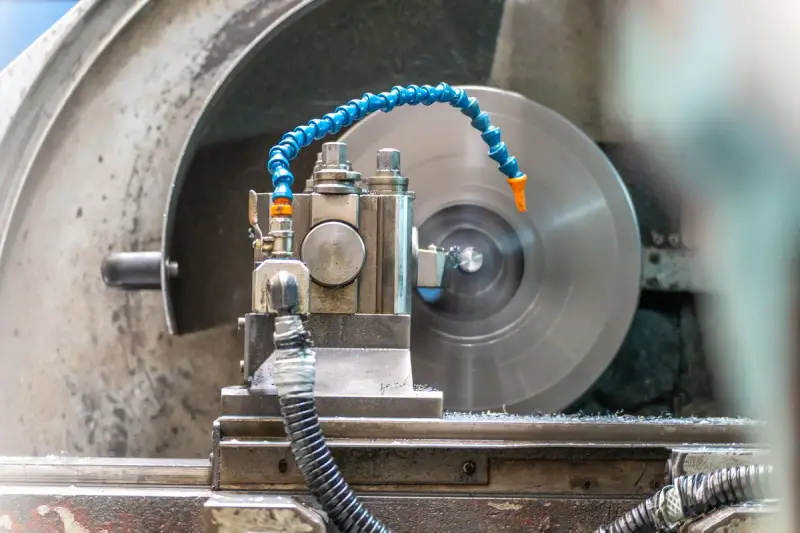 Lathe tool post with a blue coolant hose in front of a large spinning chuck in a machine shop