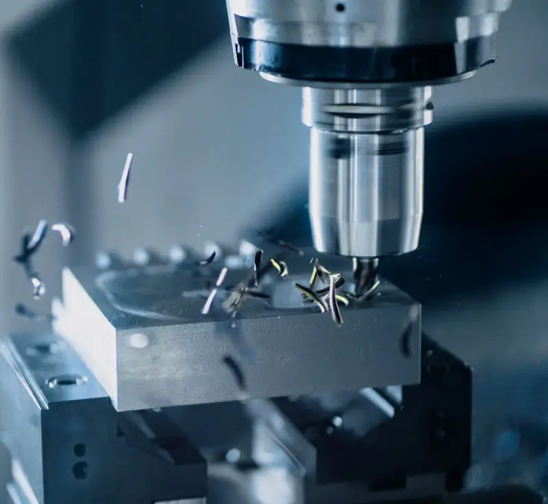 End mill cutting a pocket into an aluminum block held in a vise, with chips flying