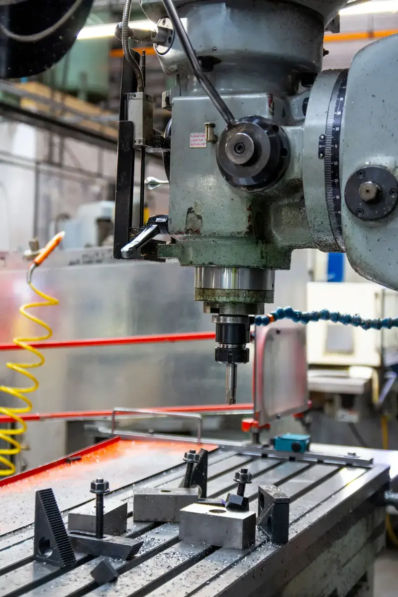 Knee milling machine head and cutter above a T-slot table with step blocks and clamps