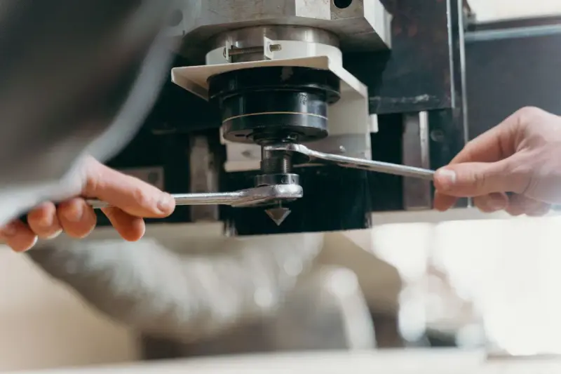 Hands using two wrenches to change the tool in a CNC spindle