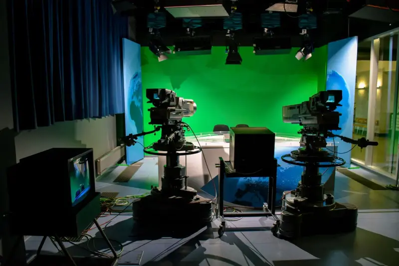 Television studio with professional video cameras on tripods facing a green screen