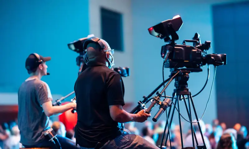 Two camera operators filming a live indoor event with professional video cameras