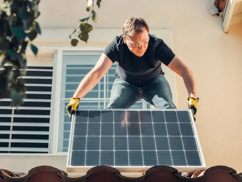 Installer in safety glasses fitting a solar panel onto a house roof