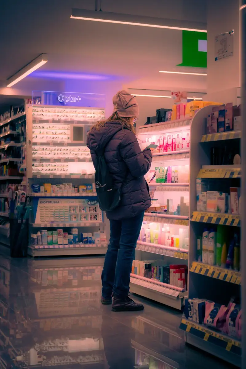 Shopper browsing lit shelves of skincare and health products in a pharmacy