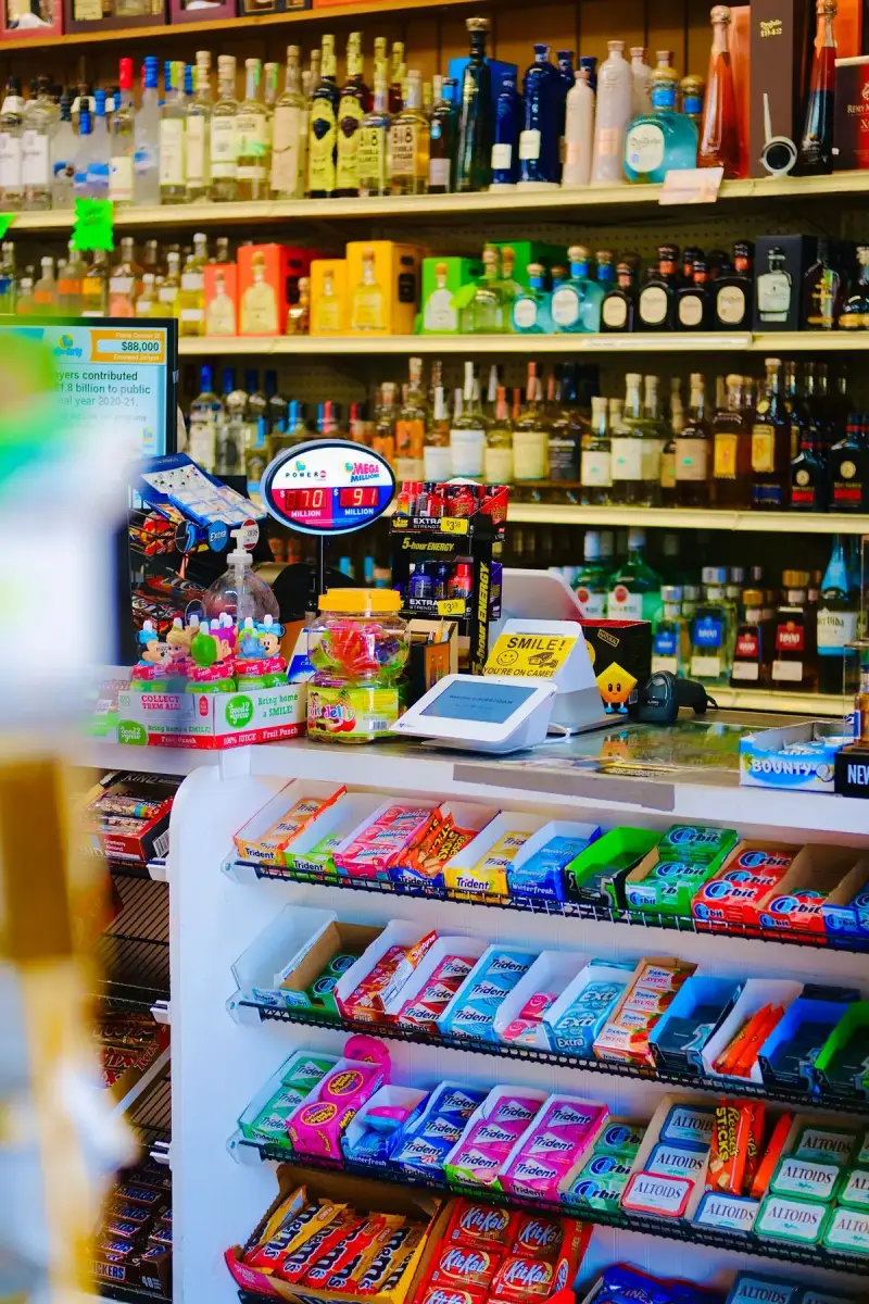 Checkout counter with gum and candy racks, a card terminal and shelves of bottles behind
