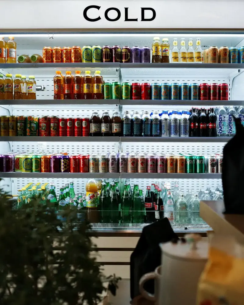 Open refrigerated case stocked with canned and bottled drinks under a sign reading Cold