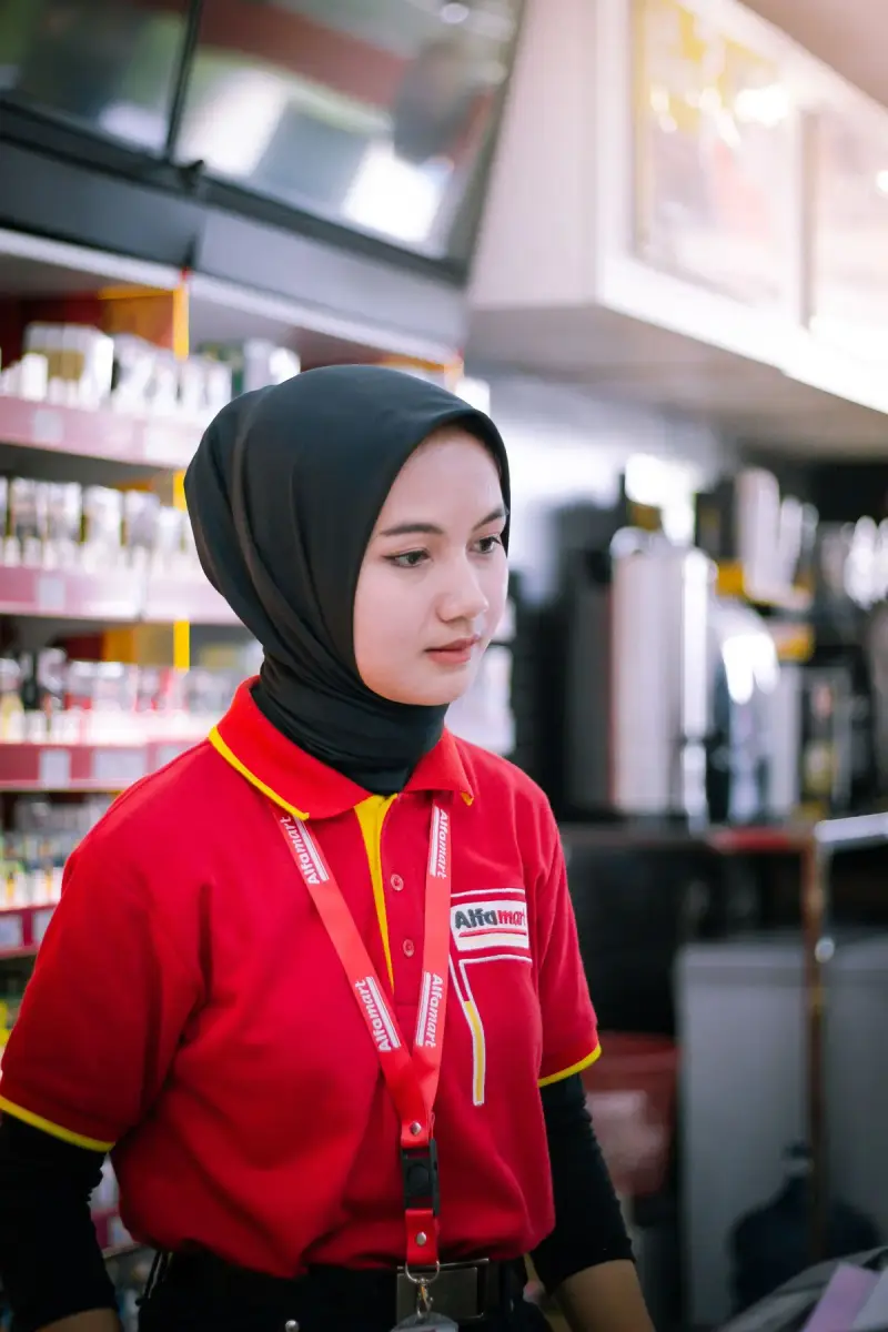 Young woman in a hijab and red uniform working the register of a convenience store