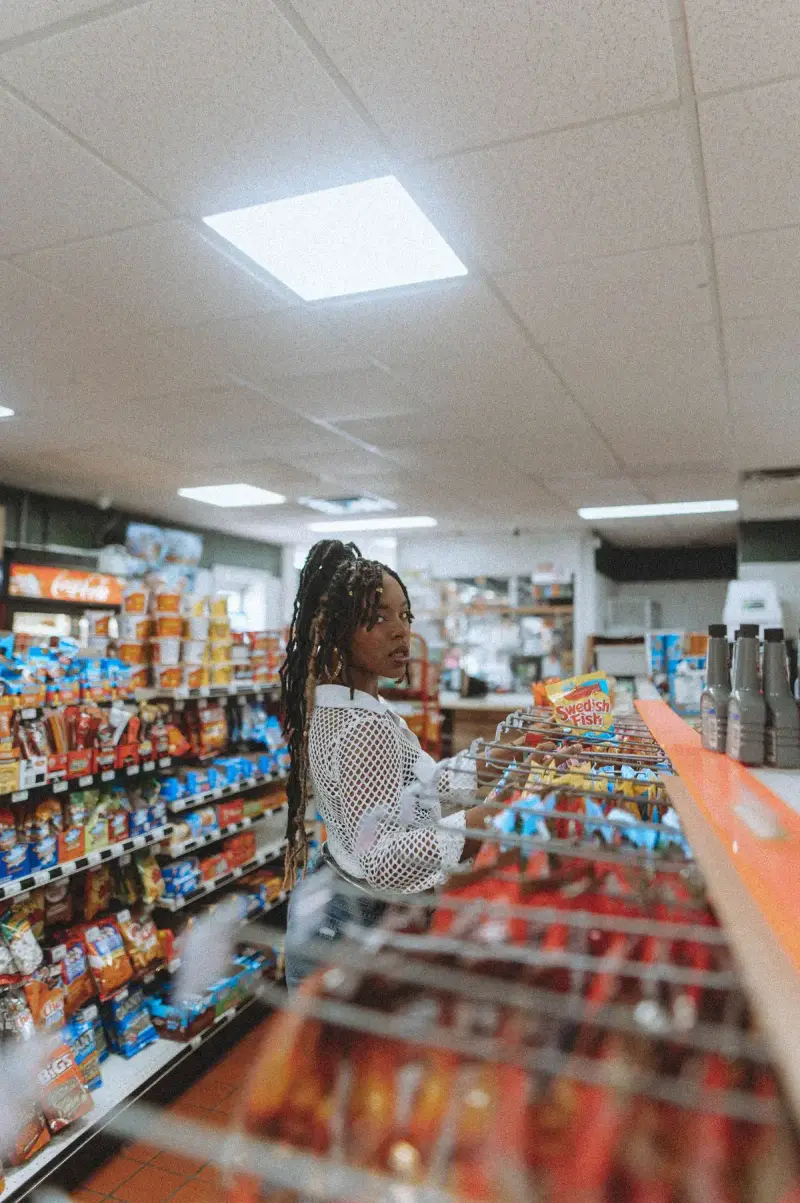 Woman choosing snacks from a packed store aisle beside the front counter