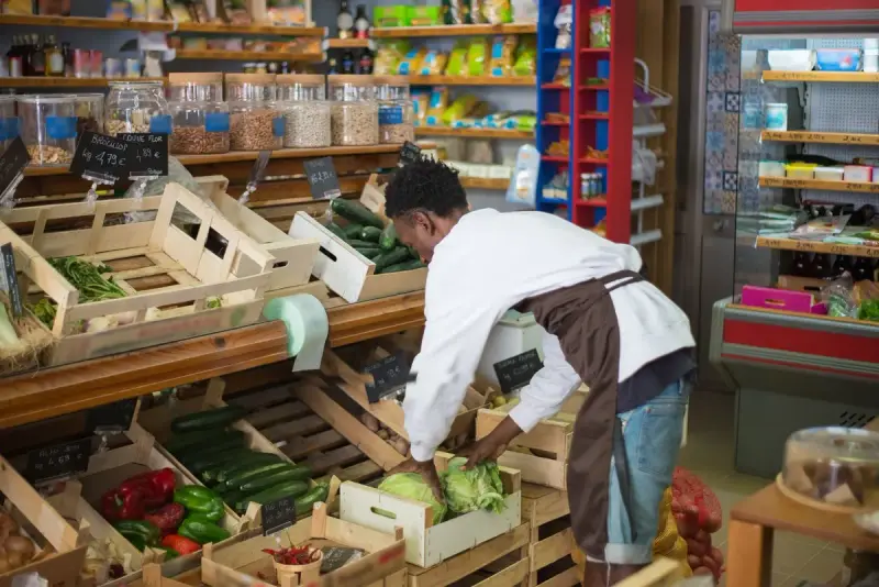 Store worker in an apron arranging fresh vegetables in wooden crates on a shop display