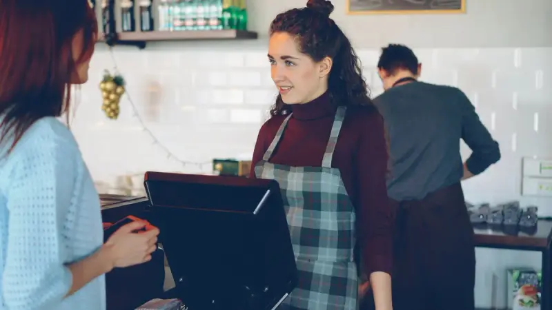 Barista in a plaid apron serving a customer at a coffee shop counter register