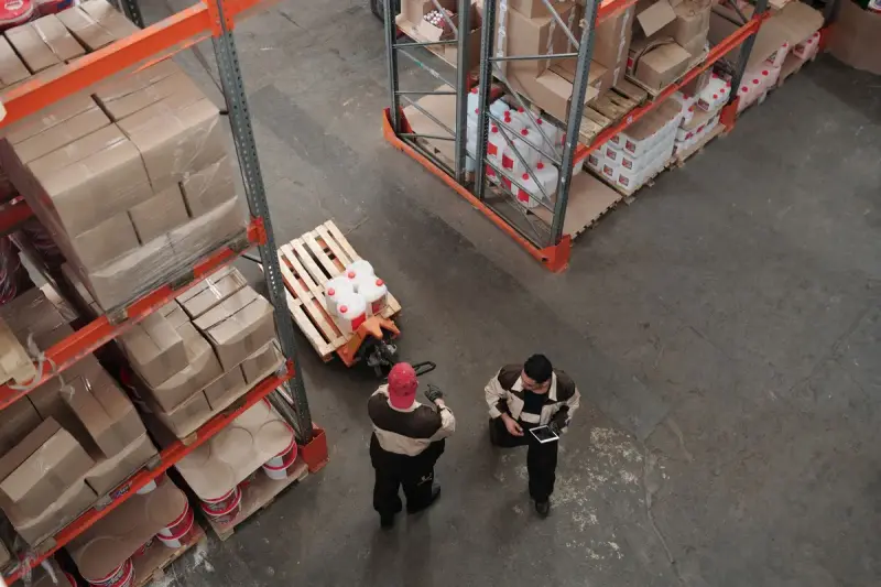 High view of two warehouse workers with a pallet jack among loaded racks