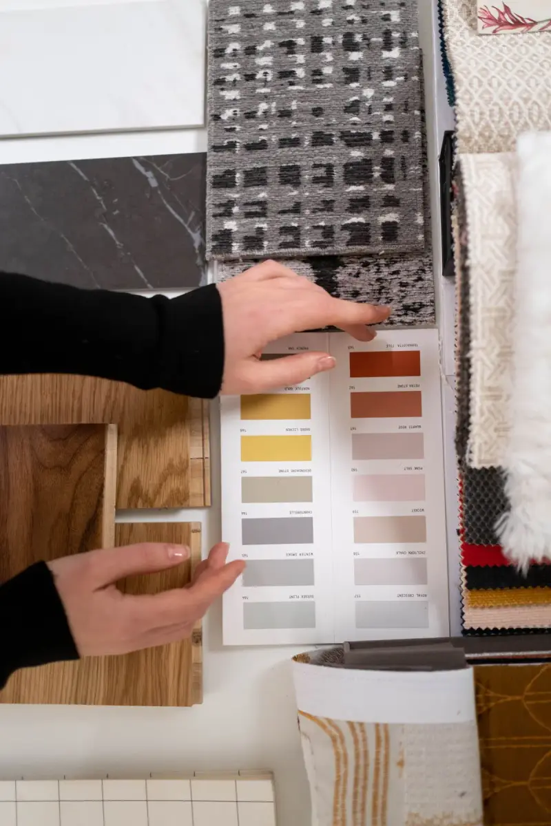 Hands choosing from color cards beside wood, stone and fabric samples