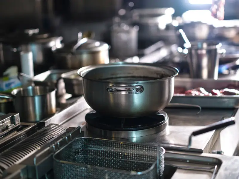 Commercial kitchen line with stainless steel cookware, work surfaces and cooking appliances