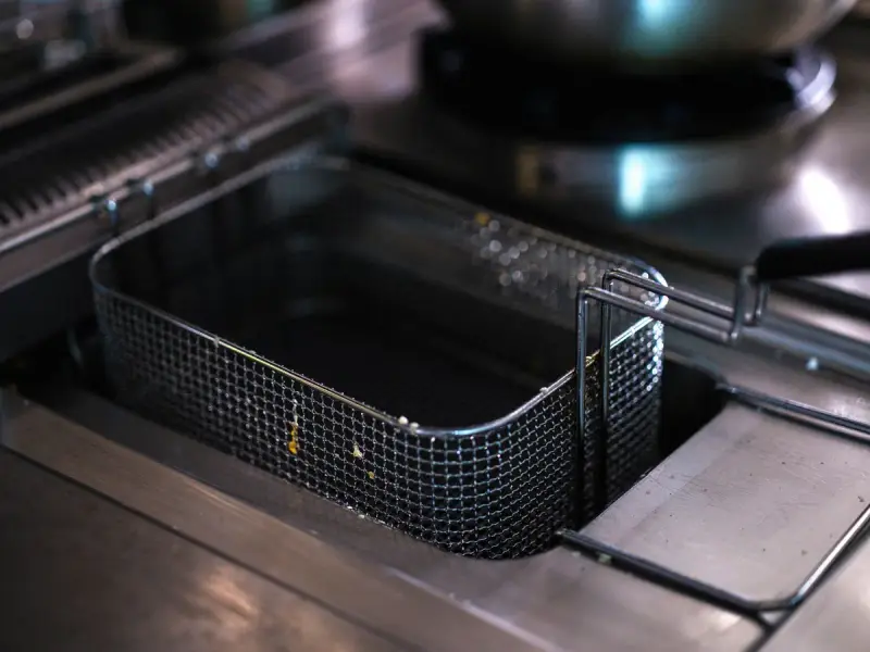 Empty deep fryer basket in a clean stainless steel commercial kitchen