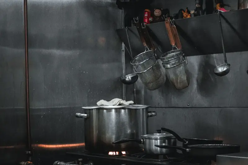 Stainless steel commercial kitchen with pots, strainers and utensils hanging on a rail