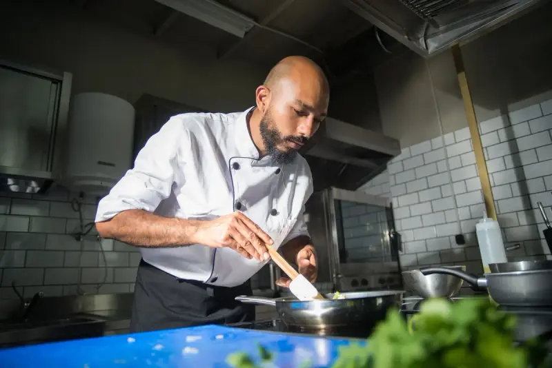 Chef in a white jacket cooking at a stainless steel range in a commercial kitchen