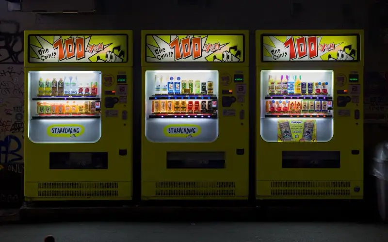 Three yellow beverage vending machines lit up at night against a dark wall