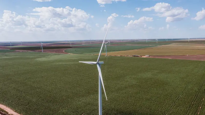 Wind turbine above wide green Texas farmland with a wind farm on the horizon