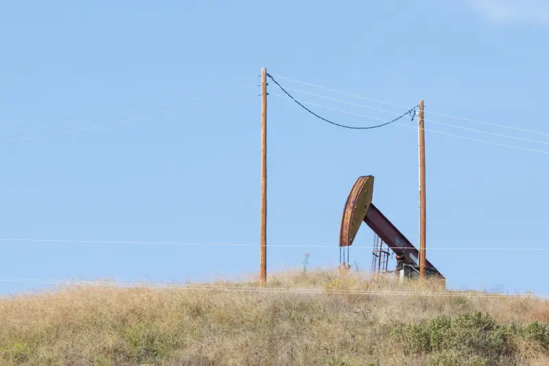 Pumpjack on a grassy rise beneath a power line and two wooden poles
