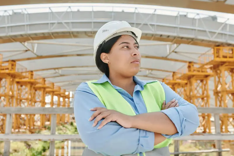 Woman engineer in a hard hat and safety vest standing with arms crossed on site