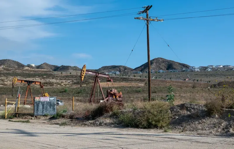 Several pumpjacks working in hilly scrubland beside utility poles