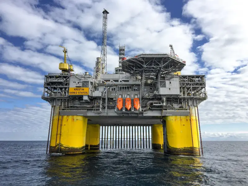 Yellow-legged offshore production platform standing in the sea under scattered clouds