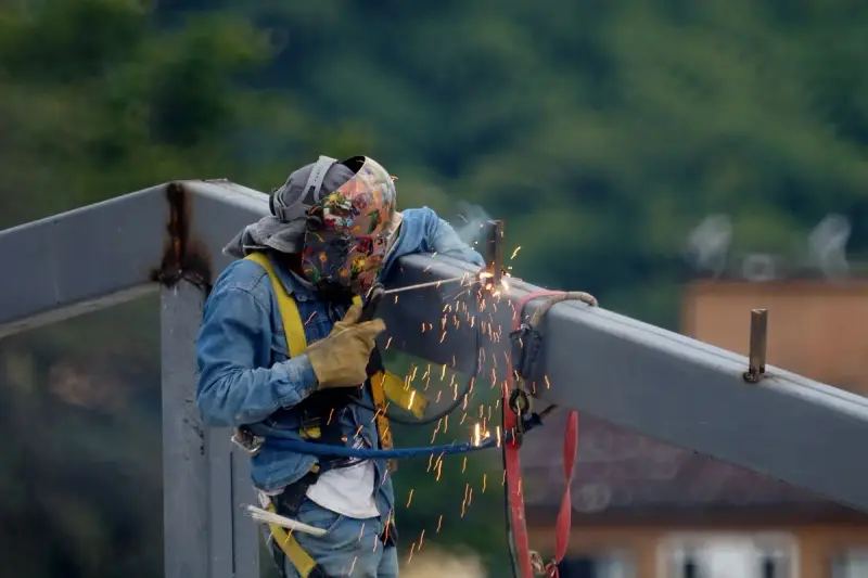 Construction worker in safety gear welding a steel beam outdoors with sparks