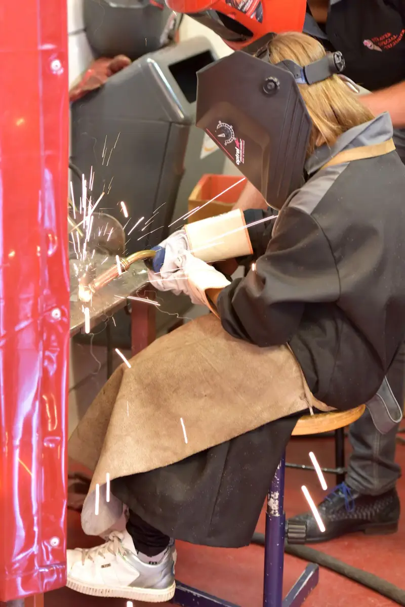 Woman welder in a protective mask working on metal as sparks fly