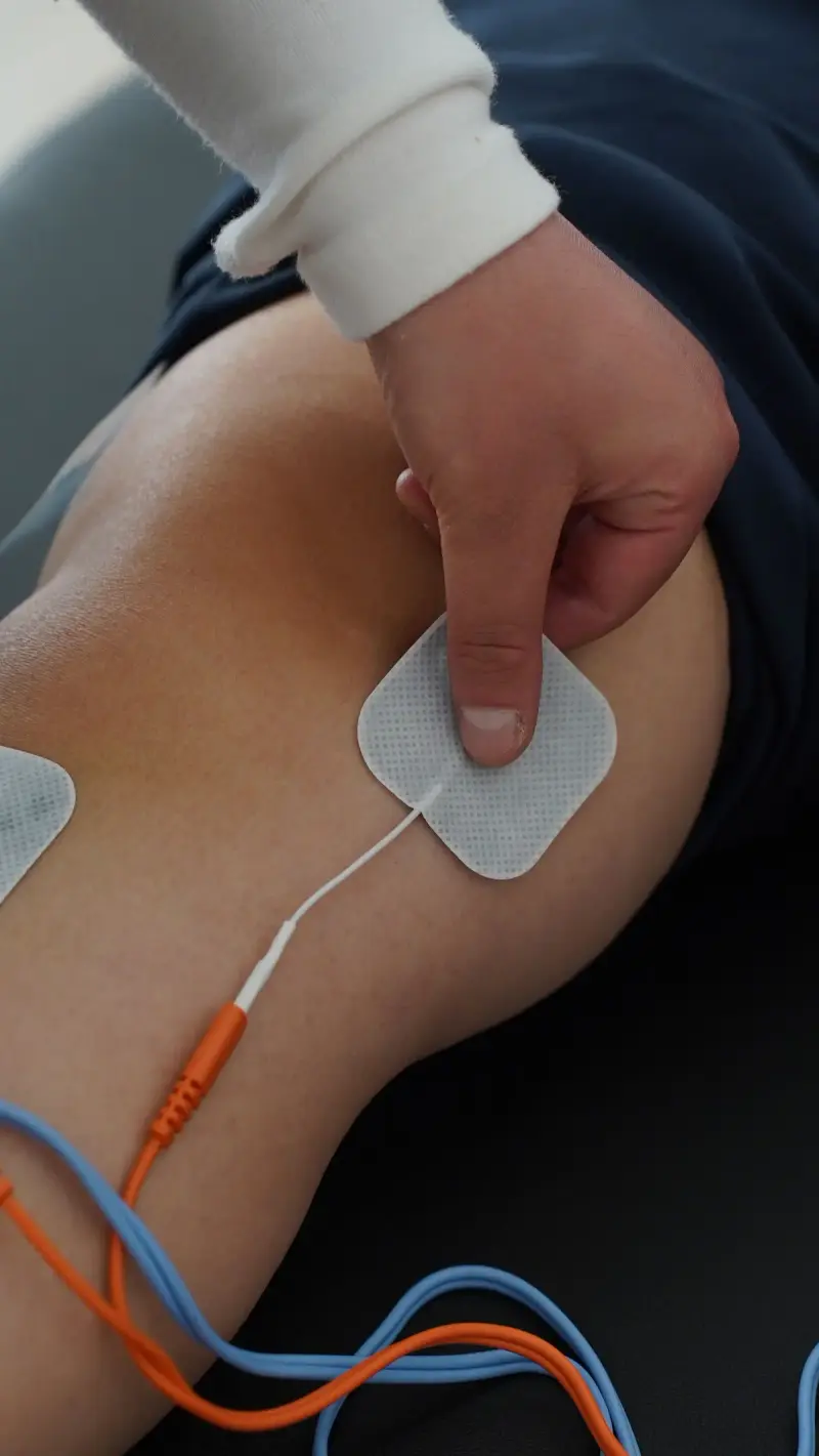 Hand pressing an electrical stimulation pad onto a knee with orange and blue lead wires