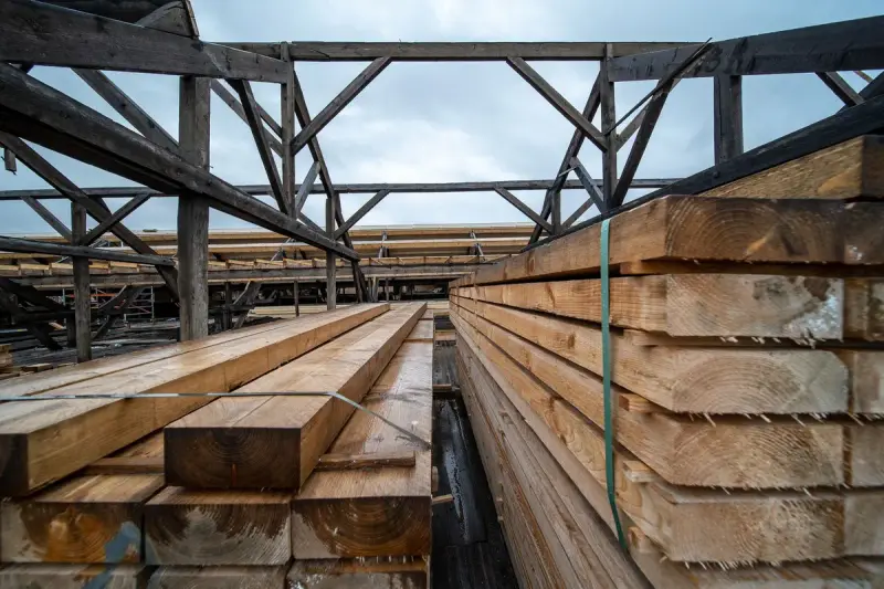 Stacked timber planks in an outdoor storage area under a cloudy sky