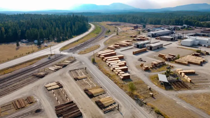 Aerial view of a sawmill and lumber yard beside forest in Jaffray, British Columbia