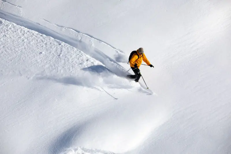Skier in a yellow jacket carving down a wide untracked snow slope