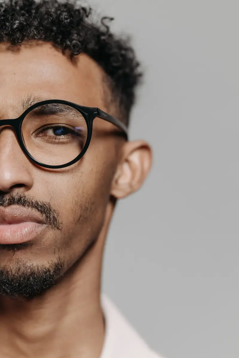 Close crop of a man in round black acetate eyeglasses on a grey background