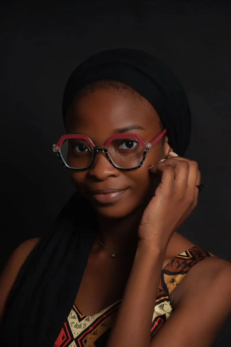 Woman in a black head wrap wearing red geometric eyeglasses, studio portrait
