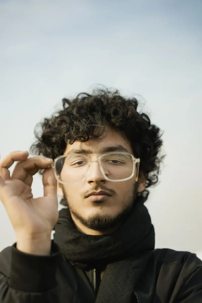 Young man with curly hair holding clear crystal eyeglass frames outdoors