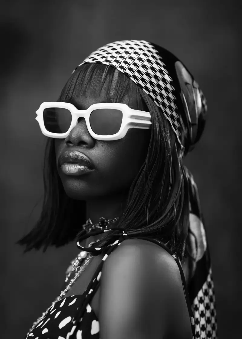 Black and white portrait of a woman in chunky white sunglasses and a patterned headscarf