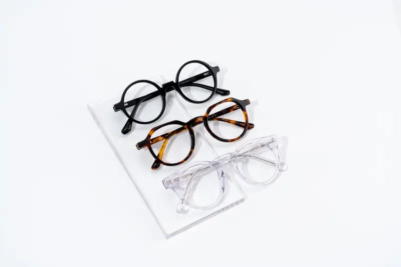 Three round eyeglass frames in black, tortoise and crystal on an acrylic stand