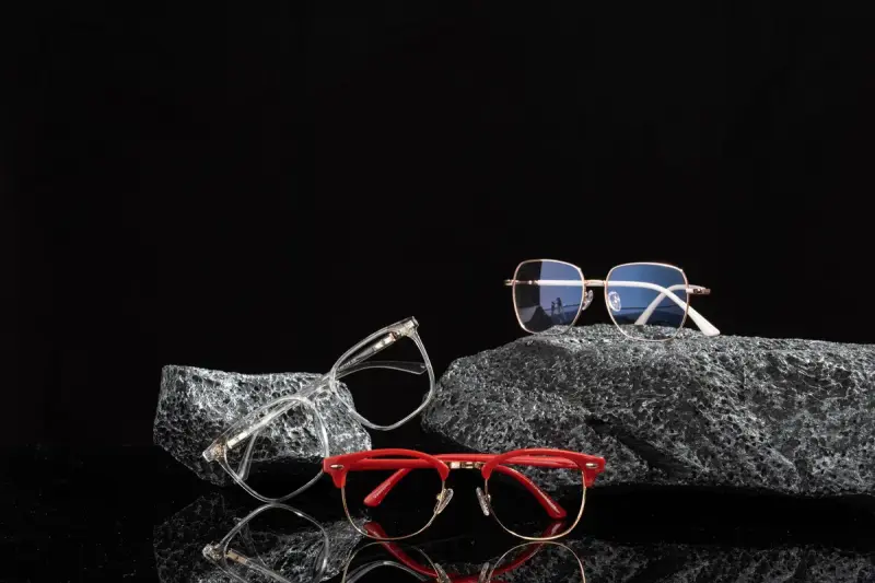 Eyeglass frames in clear, red and gold arranged on dark textured rocks