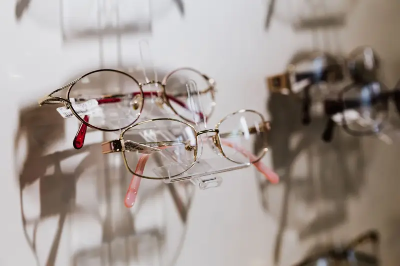 Metal eyeglass frames on clear stands along a white display wall