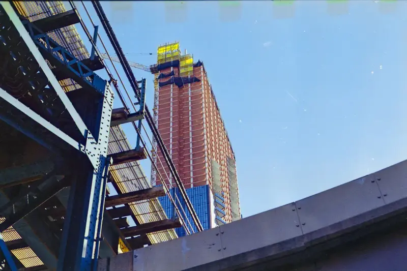 Low-angle view of a tall building under construction behind scaffolding and a steel structure