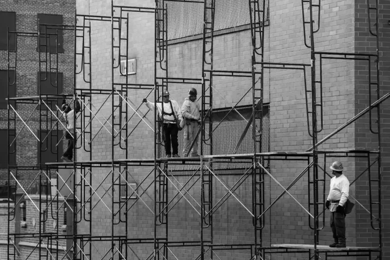 Black and white view of construction workers walking along scaffolding on a city building