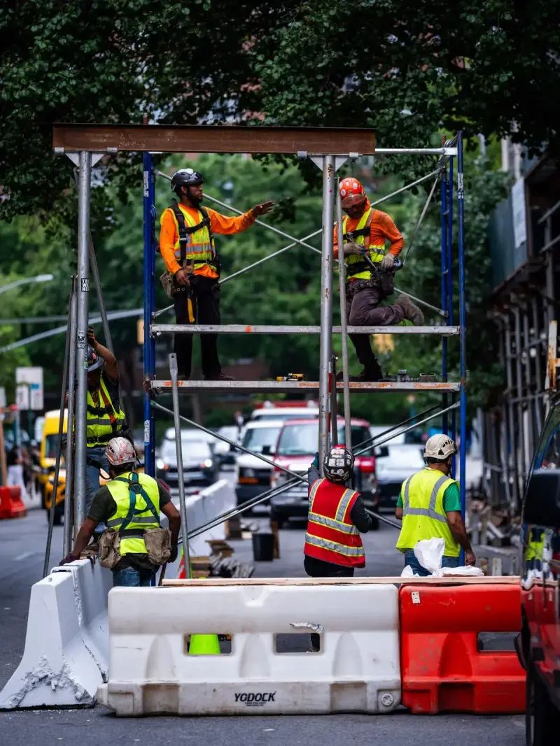 Construction workers assembling scaffolding on a city street corner