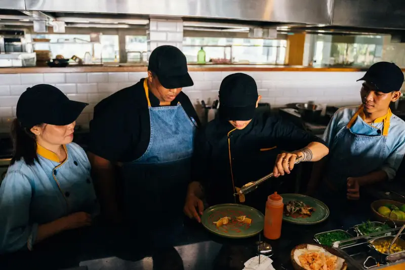 Kitchen team of women and men in caps and aprons plating dishes at a restaurant counter