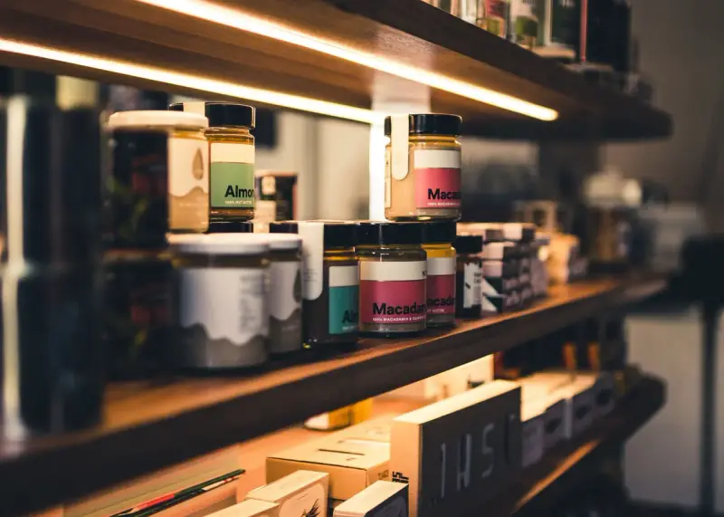 Almond and macadamia nut butter jars lined up on a wooden shelf lit from above
