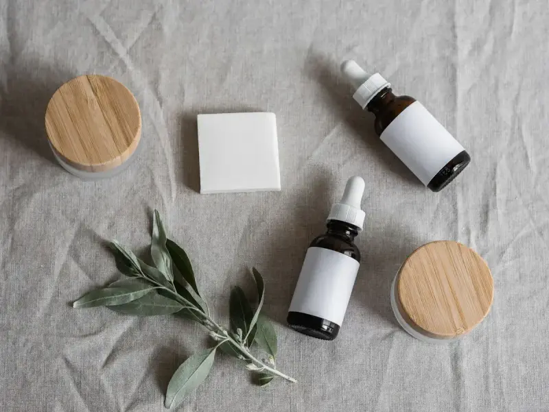 Amber dropper bottles, bamboo-lidded jars and a soap bar with olive sprigs on gray linen