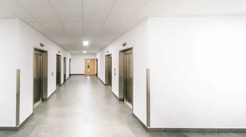 Bright office corridor with stainless steel elevator doors and polished concrete floor