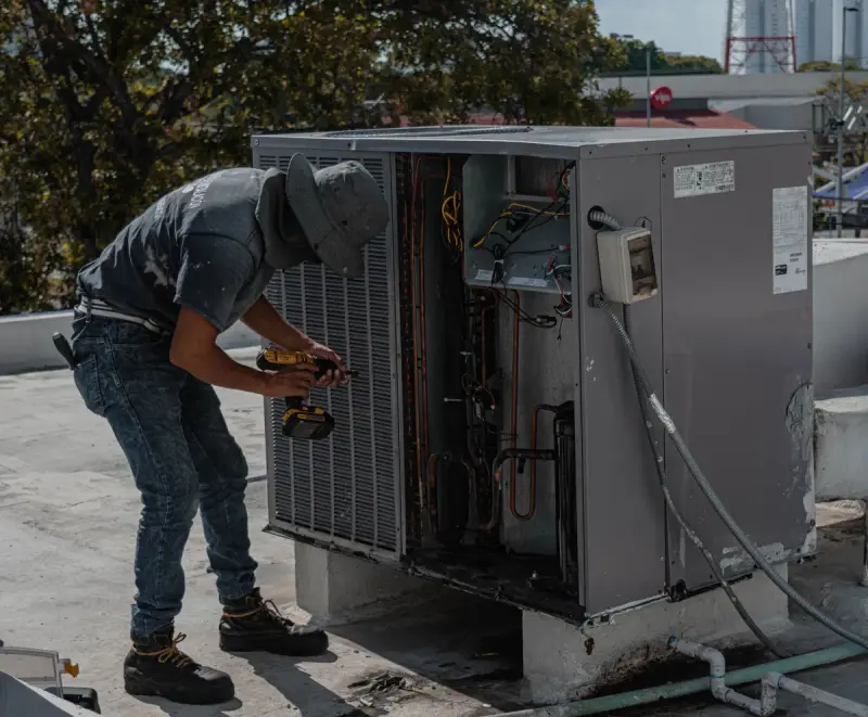 Technician working inside an open rooftop air conditioning unit with hand tools