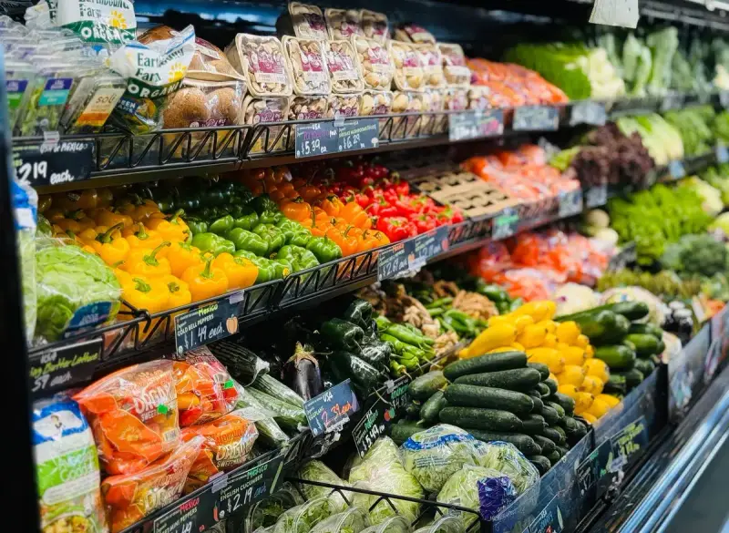 Grocery produce wall with peppers, cucumbers, squash and leafy greens on tiered shelves