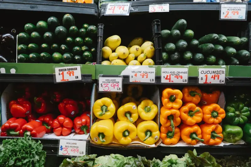 Supermarket bins of bell peppers, squash and cucumbers with handwritten price cards