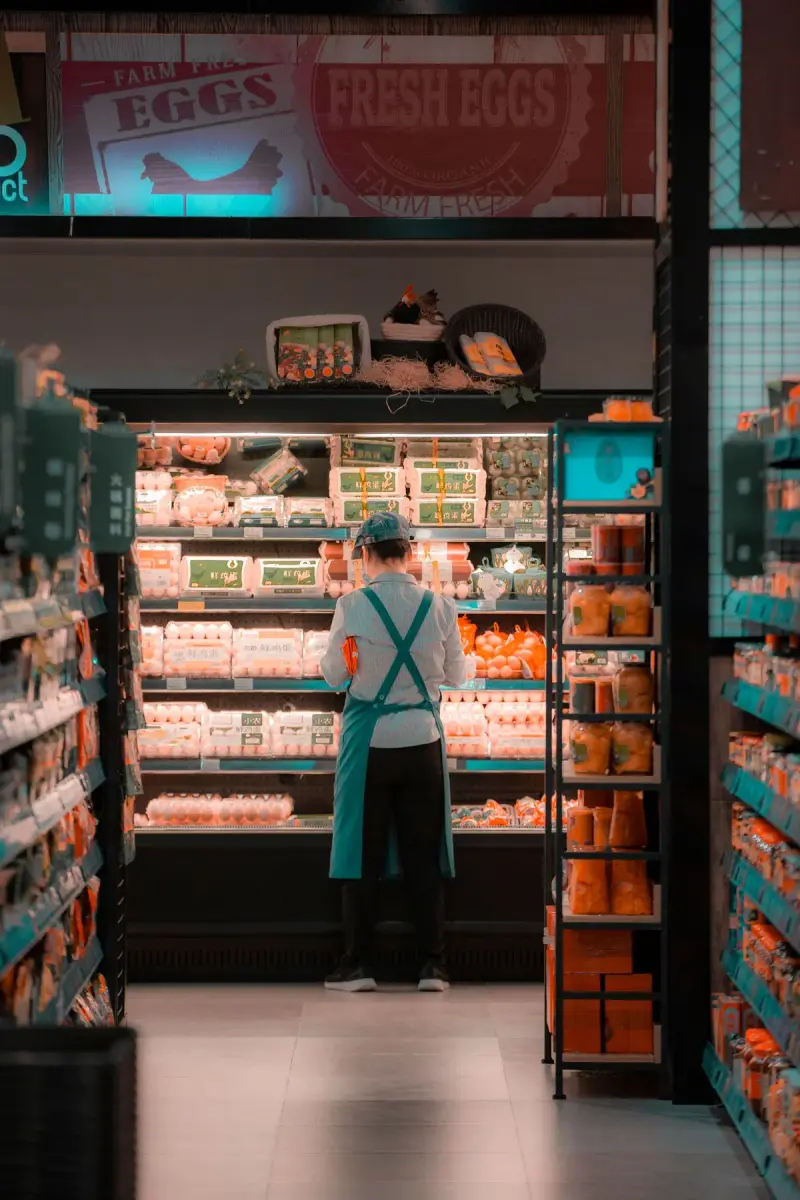 Supermarket employee in a teal apron arranging eggs in a refrigerated case